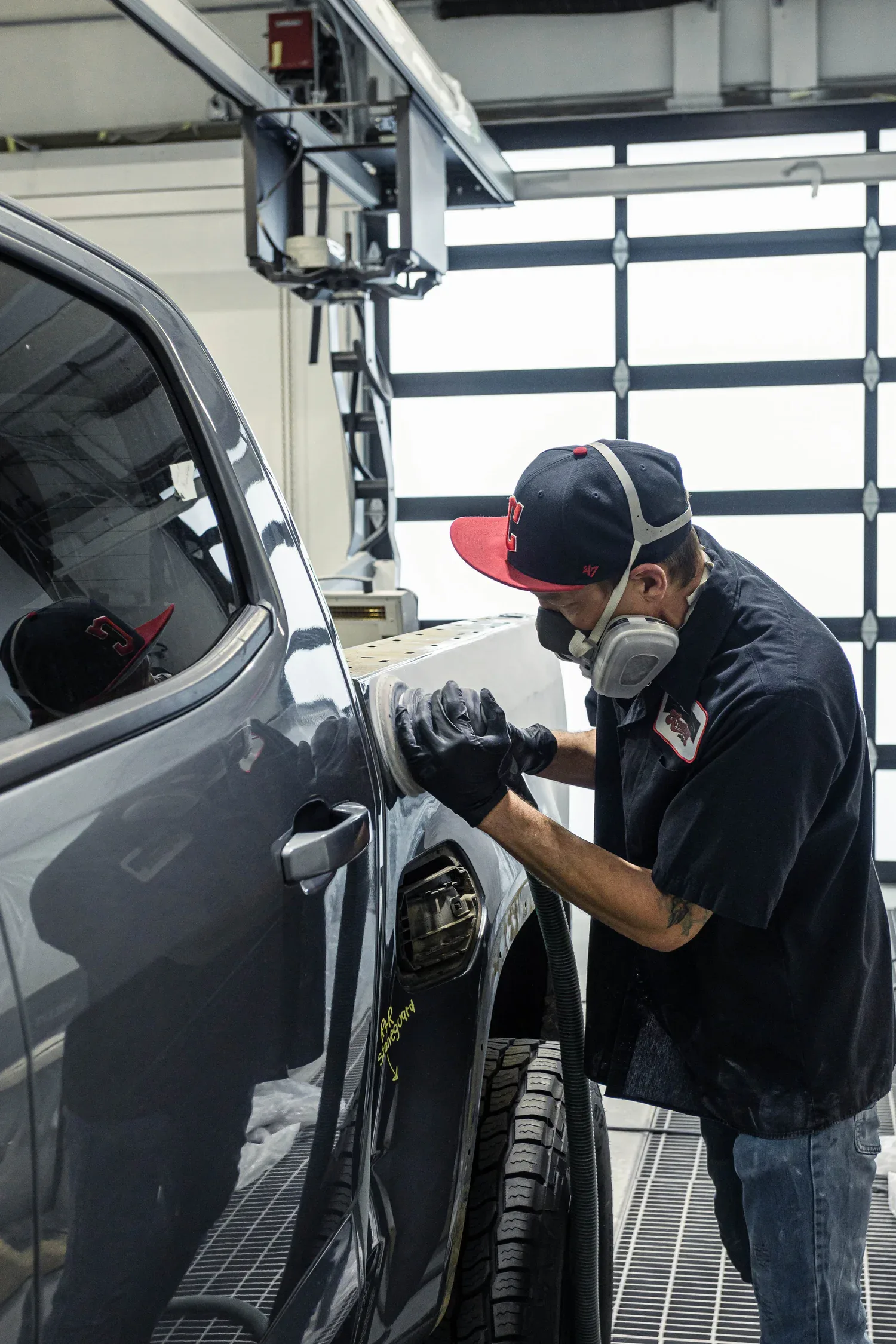A Kreations Auto Body technician in a respirator finishing a panel in the shop